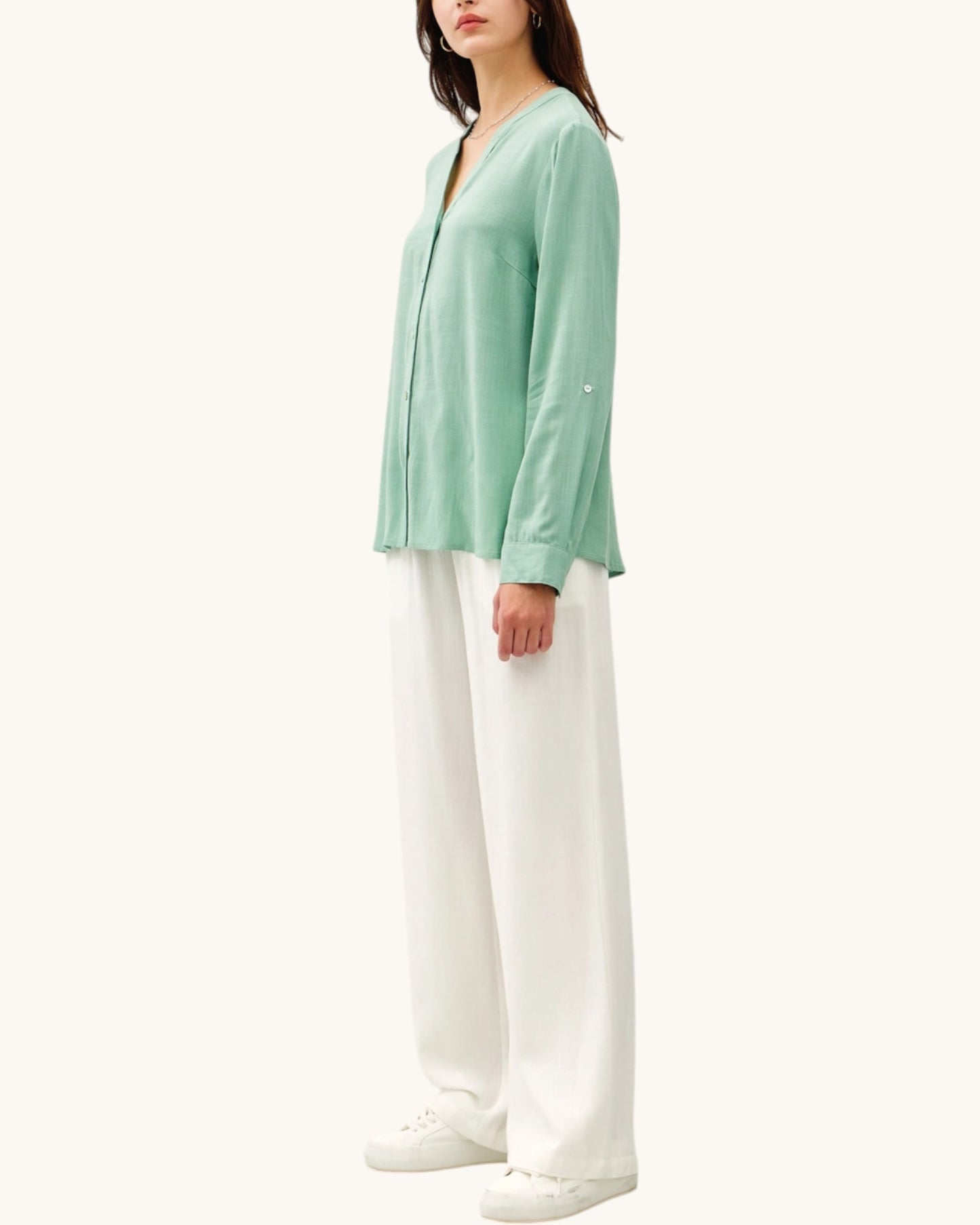 Woman wearing a light green top and white pants on a white background.