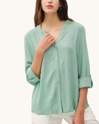 Woman wearing a light mint green button-up shirt with rolled-up sleeves on a white background.