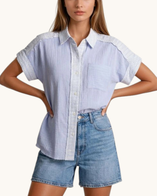 Woman wearing a light blue and white striped shirt with denim shorts on a white background.