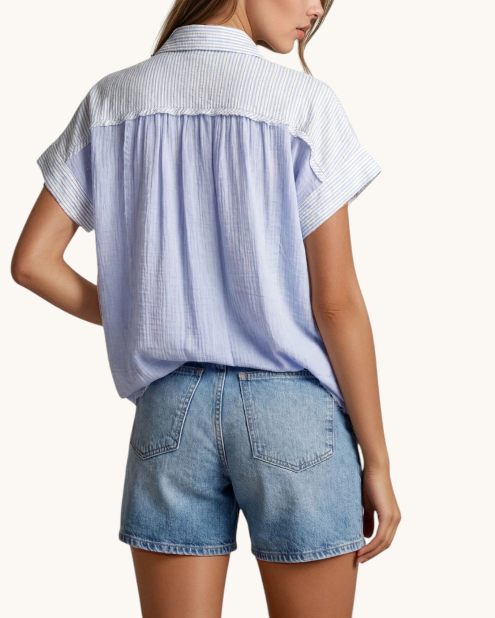 Woman wearing a light blue striped shirt and denim shorts on a white background.