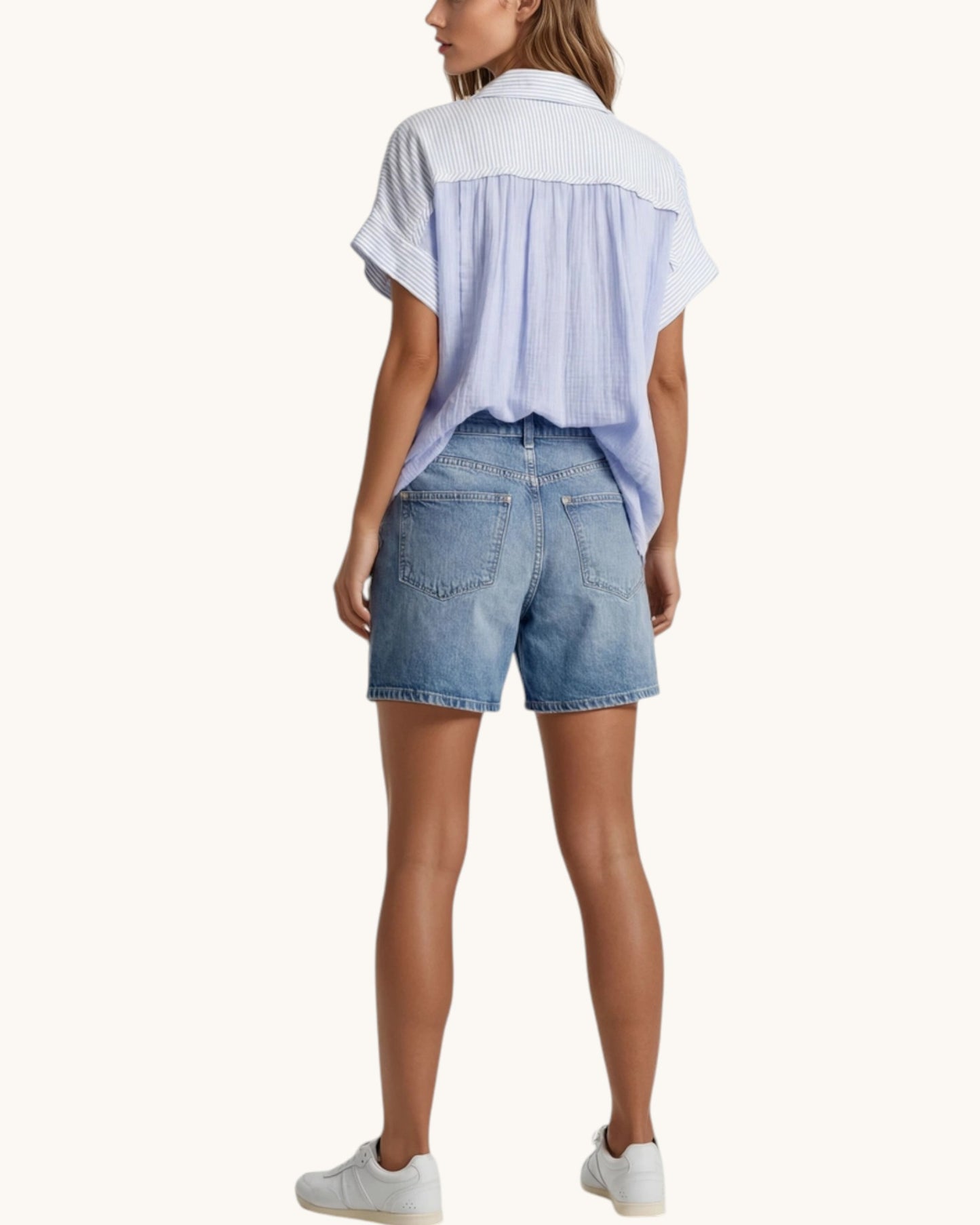 Woman wearing a light blue denim shirt and shorts on a white background.