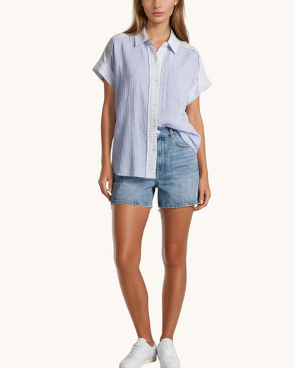 Woman wearing a light blue striped shirt and denim shorts on a white background.