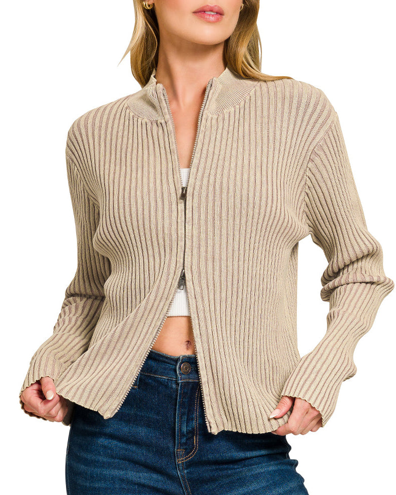 Woman wearing a light mocha ribbed zip up sweater over a white top and blue jeans on a white background.