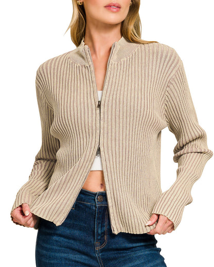 Woman wearing a light mocha ribbed zip up sweater over a white top and blue jeans on a white background.