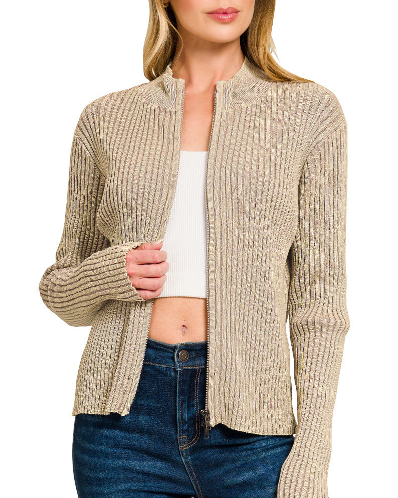 Woman wearing a light mocha ribbed zip up sweater over a white top and blue jeans on a white background.