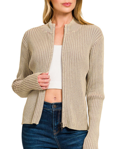 Woman wearing a light mocha ribbed zip up sweater over a white top and blue jeans on a white background.