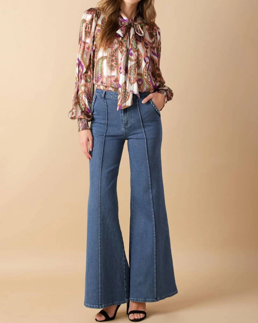Woman wearing a floral blouse and blue flared jeans on a beige background.