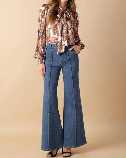 Woman wearing a floral blouse and blue flared jeans on a beige background.