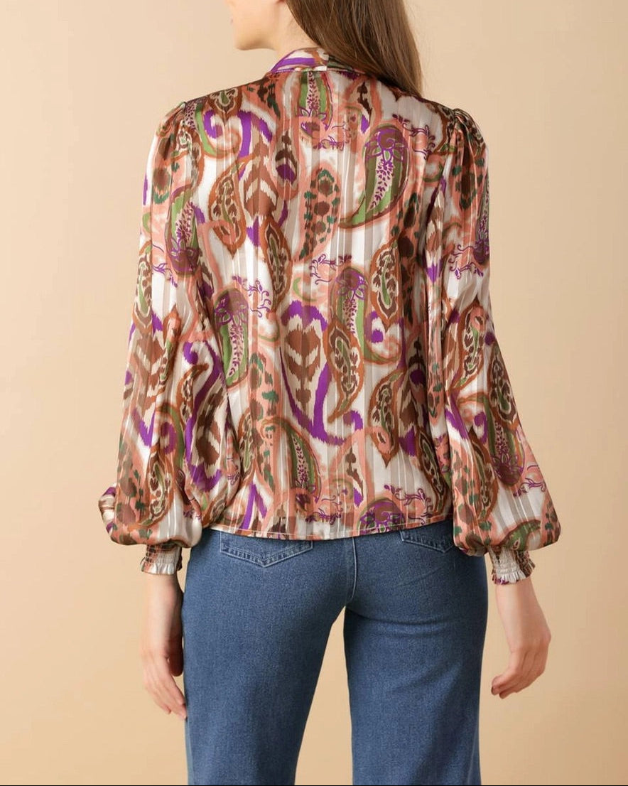 Woman wearing a patterned blouse and blue jeans on a beige background.