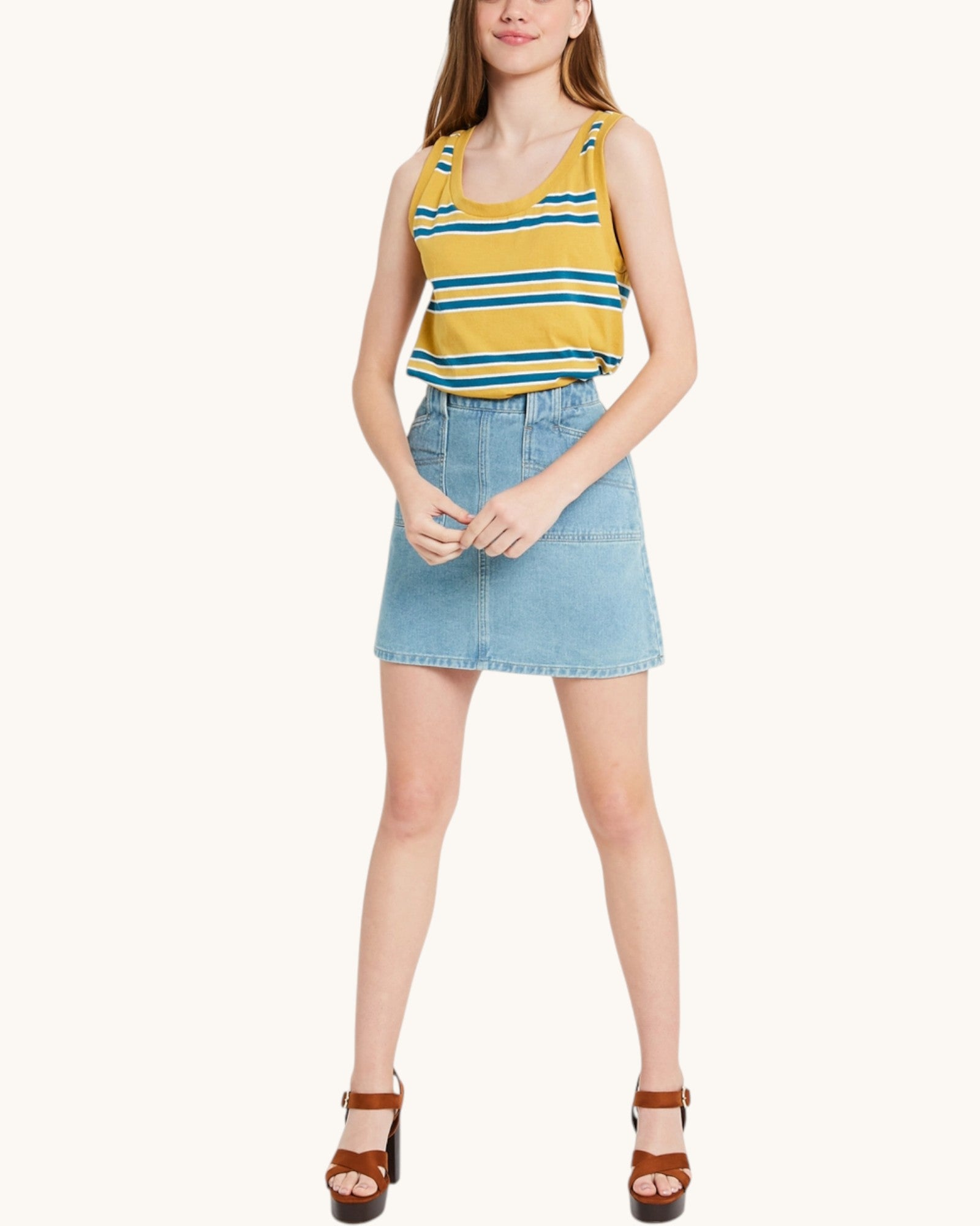 Woman wearing a yellow striped tank top and denim skirt and brown sandals on a white background.