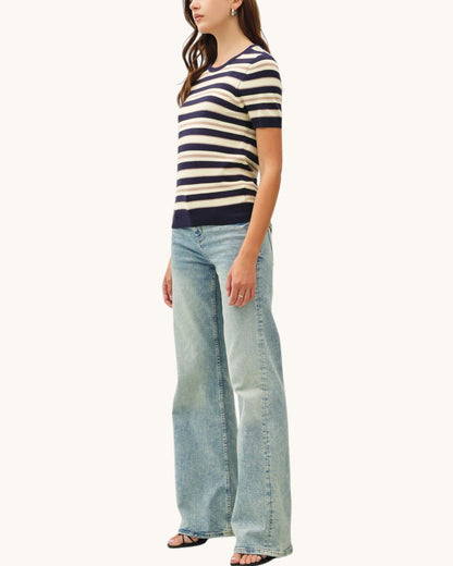 Woman wearing a striped short sleeve sweater and wide-leg jeans on a white background.