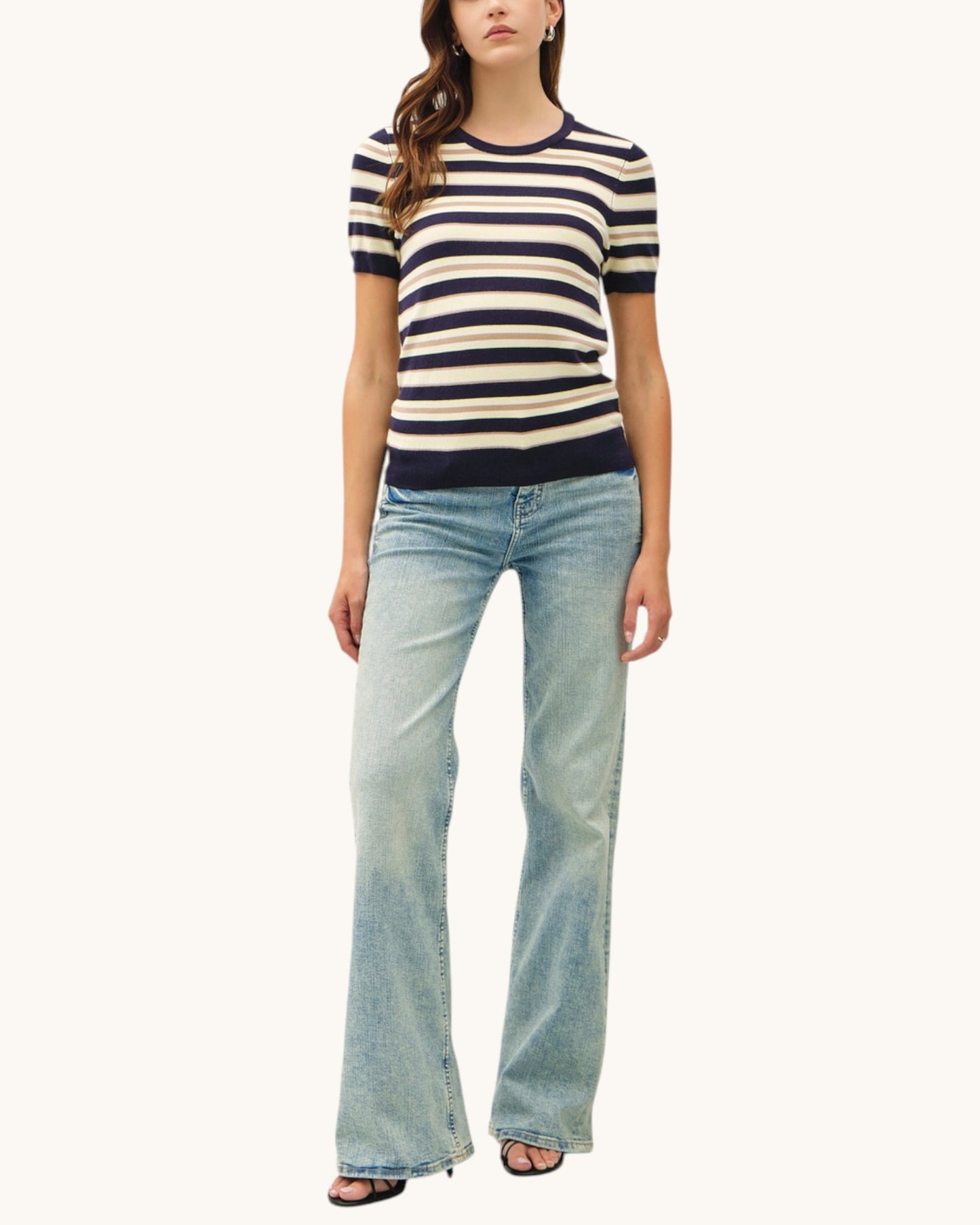 Woman wearing a navy striped short sleeve sweater and jeans on a white background.