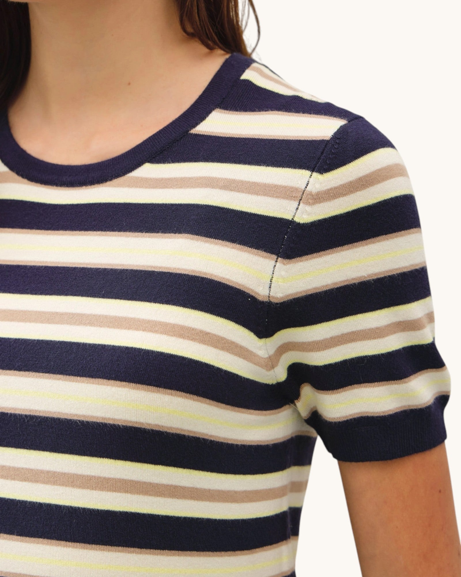Close-up of a person wearing a striped sweater with navy, beige, and white horizontal stripes.