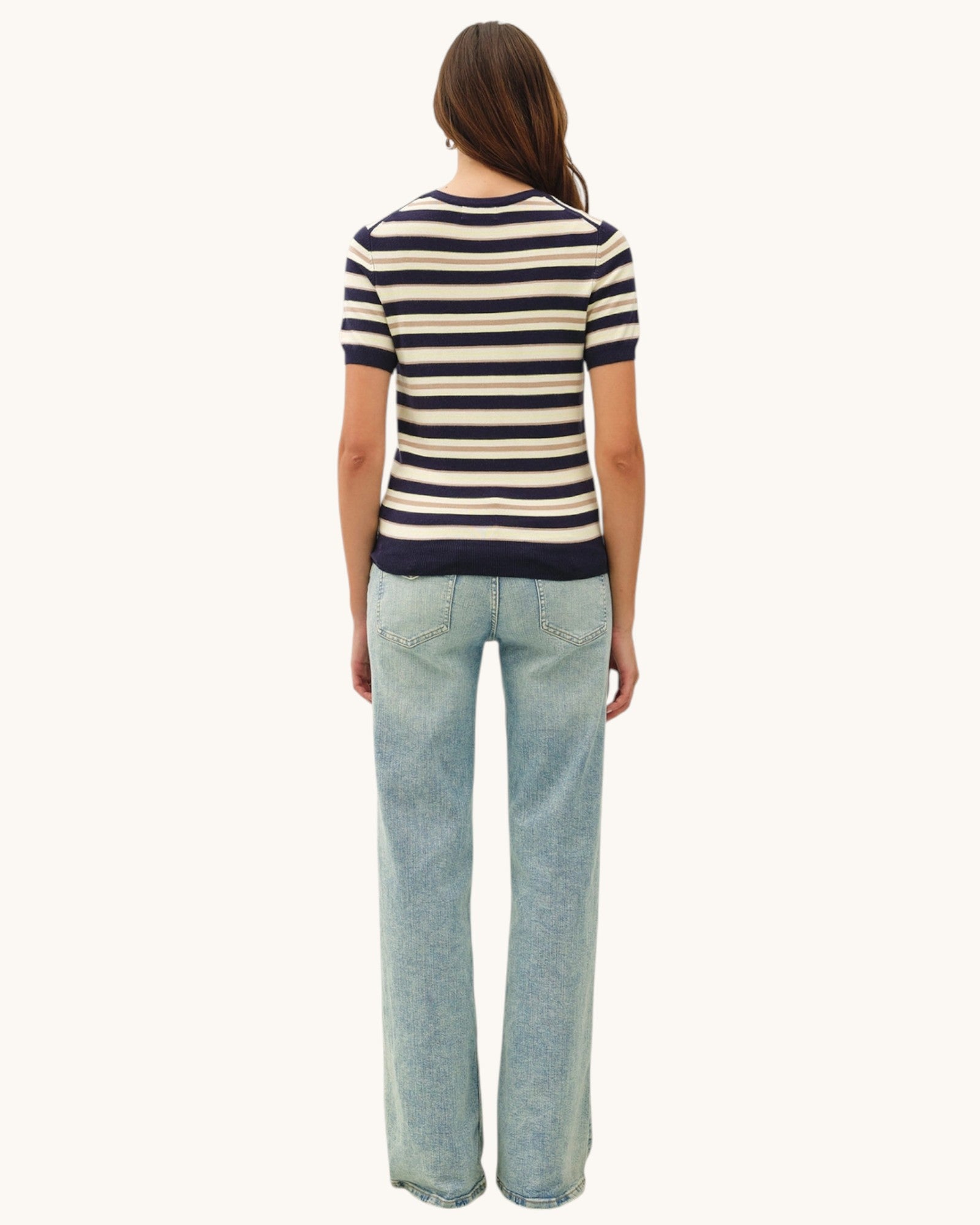 Person wearing a striped short sleeve sweater and light blue jeans on a white background.
