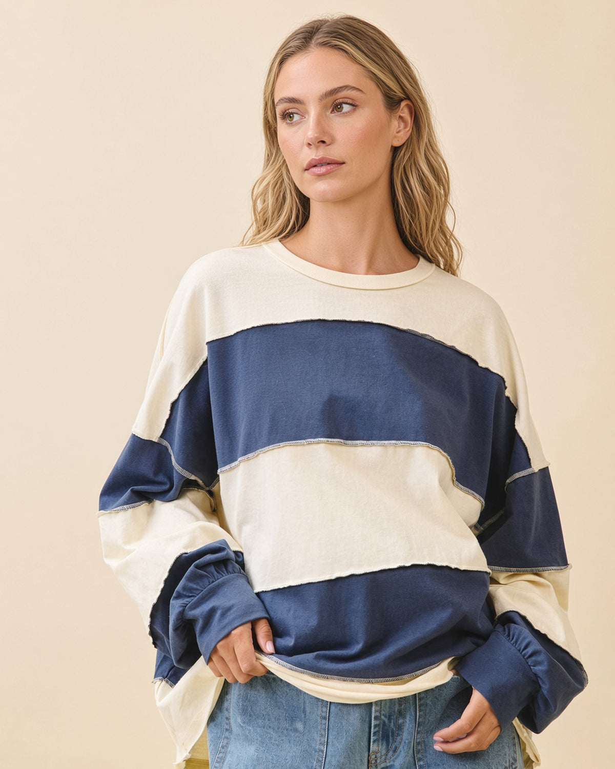 Model wearing an oversized navy and butter color block pullover with exposed seams and long sleeves.