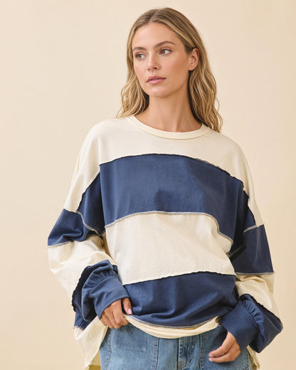 Model wearing an oversized navy and butter color block pullover with exposed seams and long sleeves.
