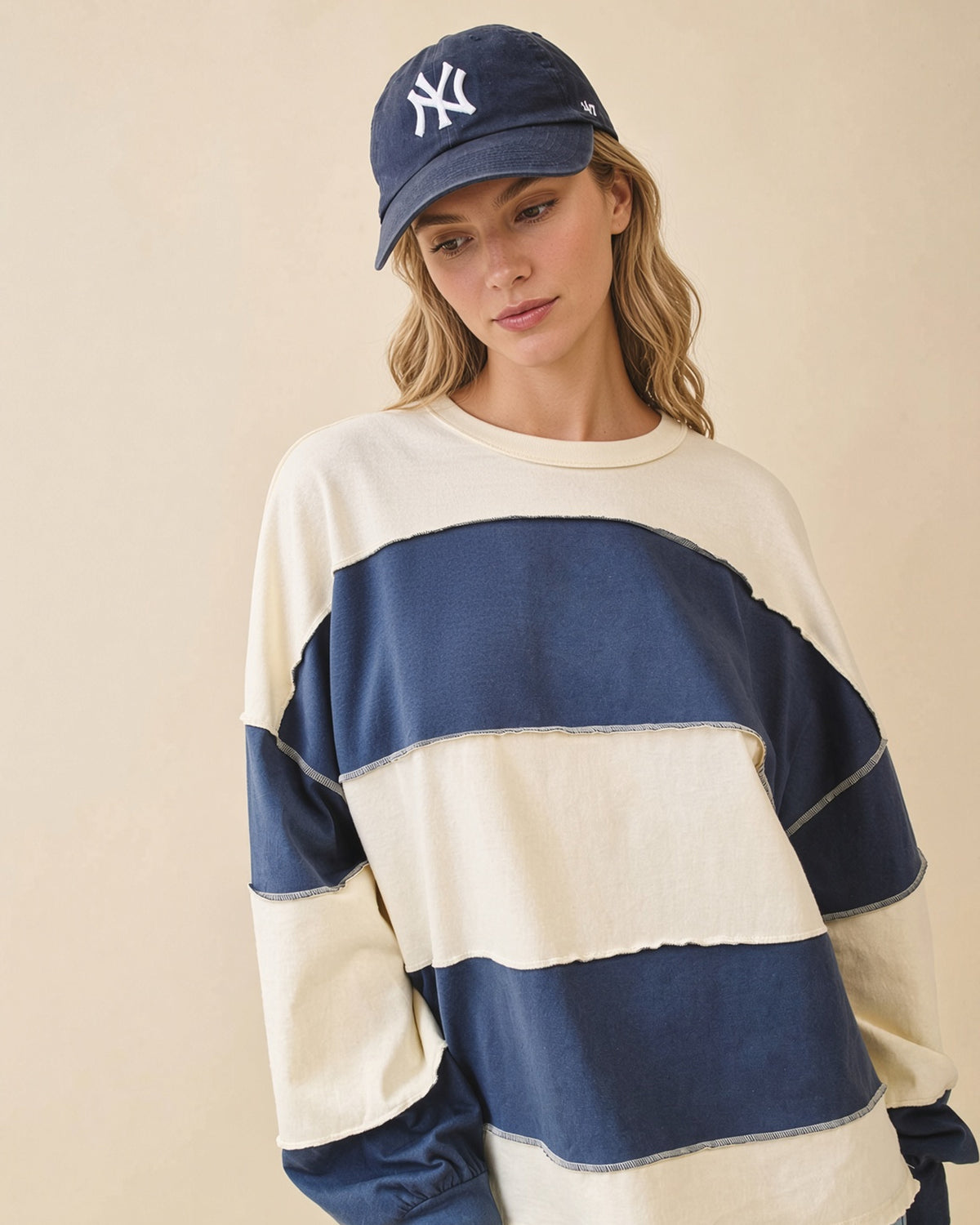 Model wearing an oversized navy and butter color block pullover with exposed seams and long sleeves.
