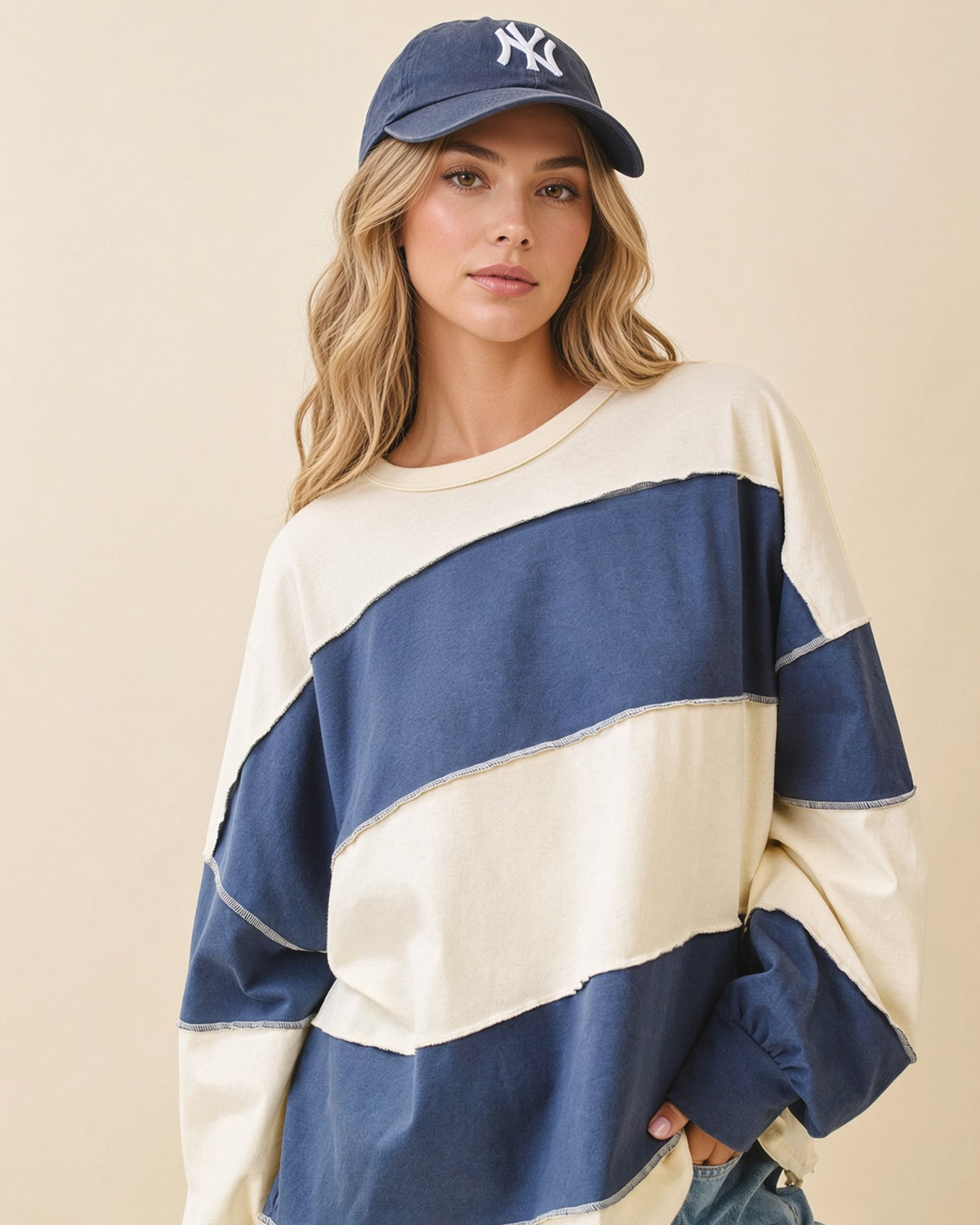 Model wearing an oversized navy and butter color block pullover with exposed seams and long sleeves.