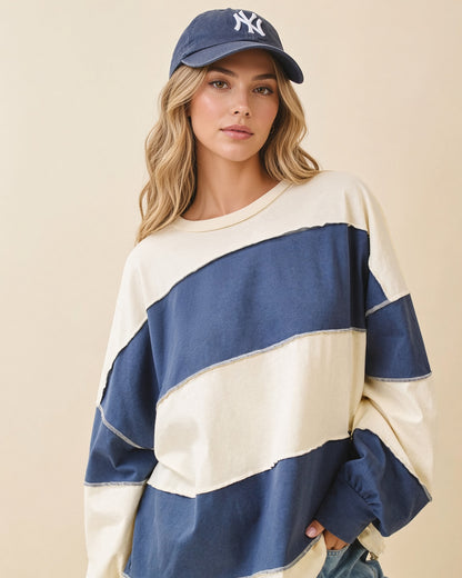 Model wearing an oversized navy and butter color block pullover with exposed seams and long sleeves.