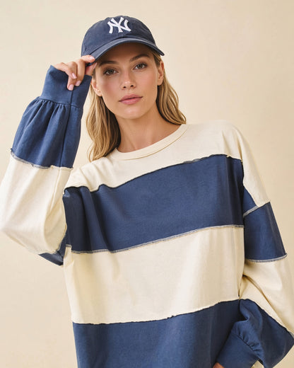 Model wearing an oversized navy and butter color block pullover with exposed seams and long sleeves.