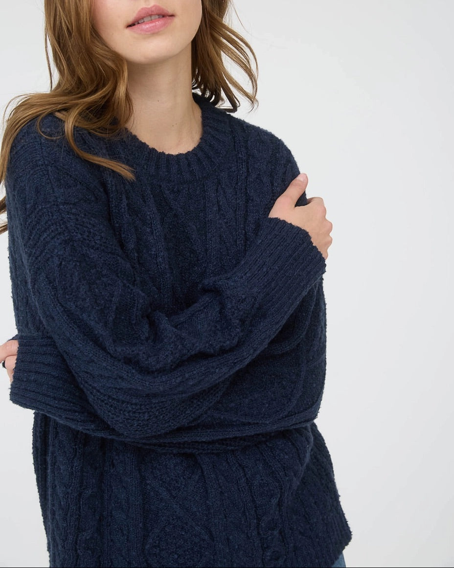 Woman wearing a navy blue chunky cable knit sweater against a white background. 