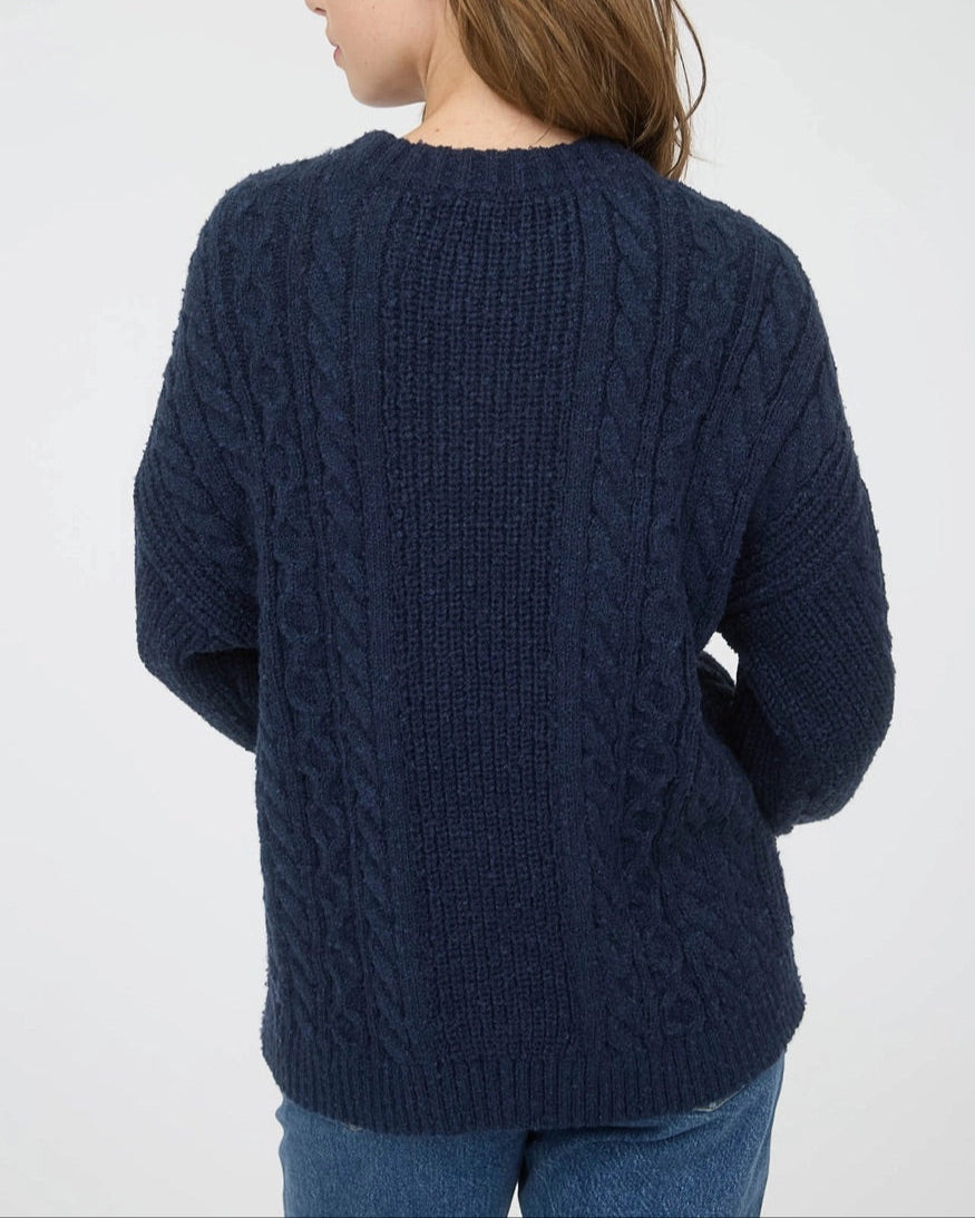 Woman wearing a navy blue chunky cable knit sweater against a white background. 