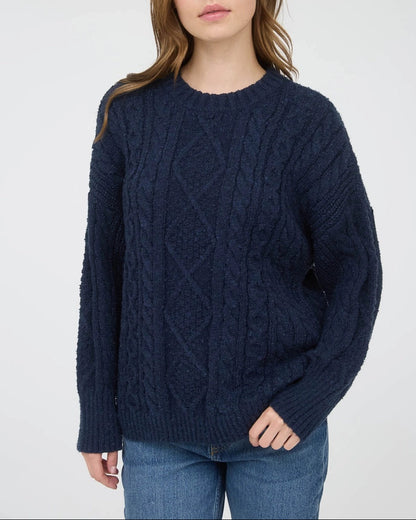 Woman wearing a navy blue chunky cable knit sweater against a white background.