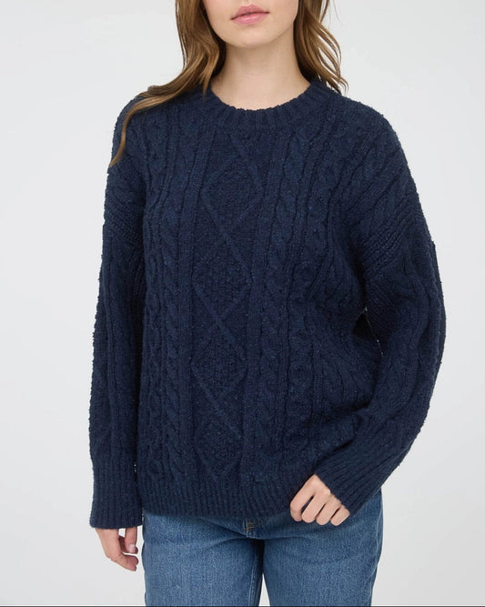 Woman wearing a navy blue chunky cable knit sweater against a white background.