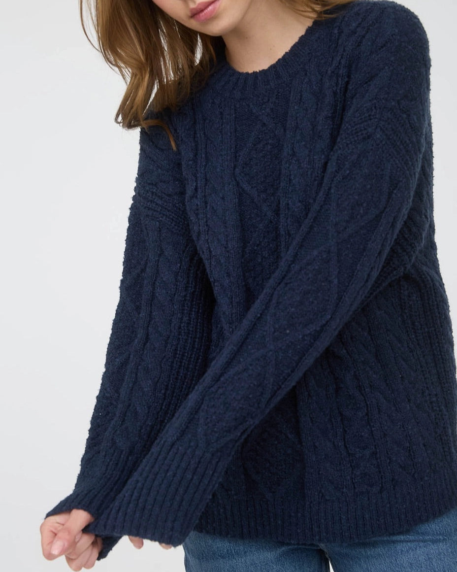 Woman wearing a navy blue chunky cable knit sweater against a white background. 