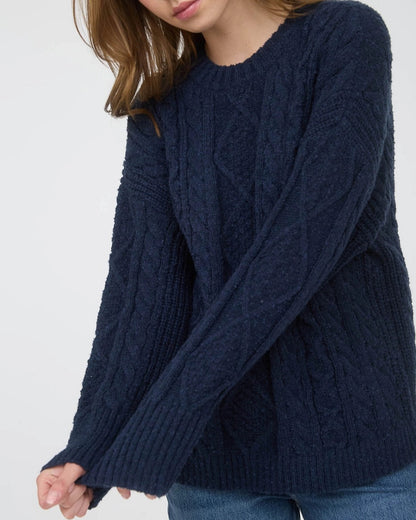 Woman wearing a navy blue chunky cable knit sweater against a white background. 