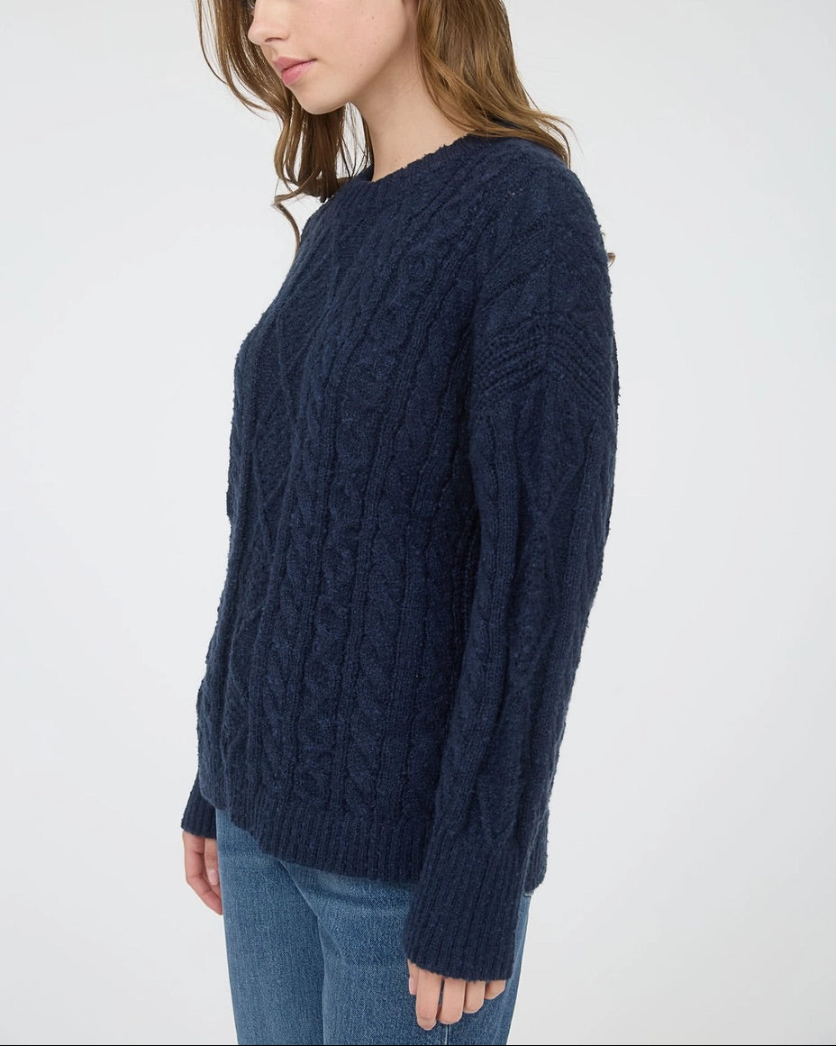 Woman wearing a navy blue chunky cable knit sweater against a white background.