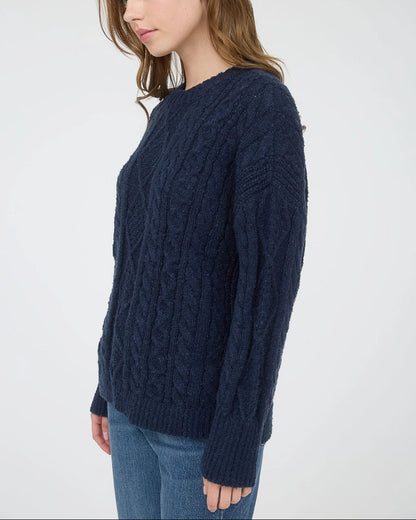 Woman wearing a navy blue chunky cable knit sweater against a white background.
