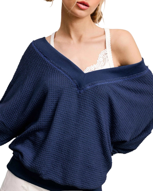 Woman wearing a navy blue oversized dual V sweater over a white top. 