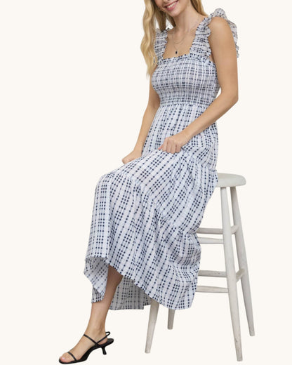 Woman wearing a blue and white checkered dress sitting on a white stool against a white background.