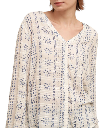 Woman wearing a textured ivory blouse with blue print and denim shorts on a white background.