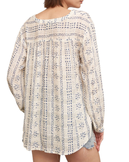 Woman wearing a textured ivory blouse with blue print and denim shorts on a white background.