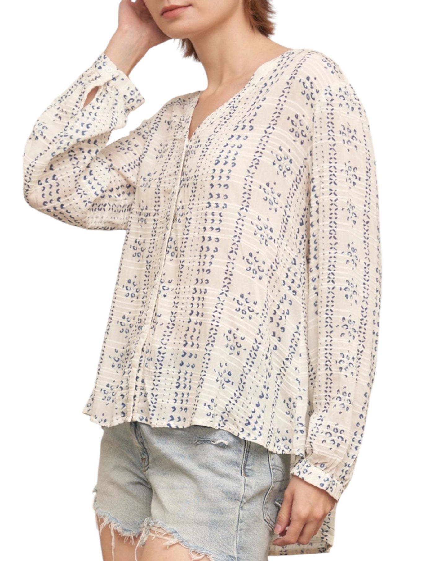 Woman wearing a textured ivory blouse with blue print and denim shorts on a white background.