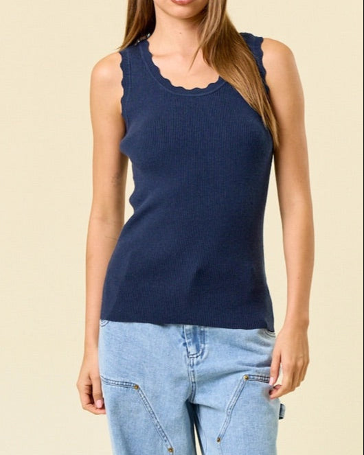 Woman wearing a navy blue sleeveless ribbed top and light blue jeans against a beige background.