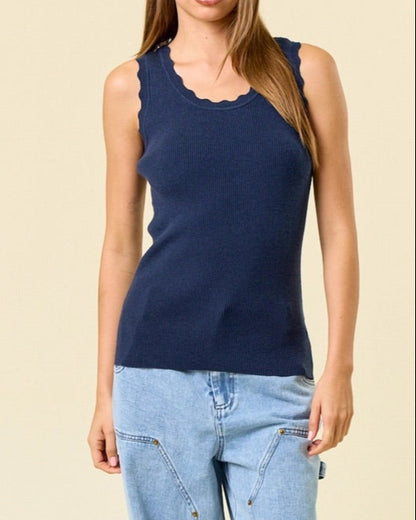 Woman wearing a navy blue sleeveless ribbed top and light blue jeans against a beige background.