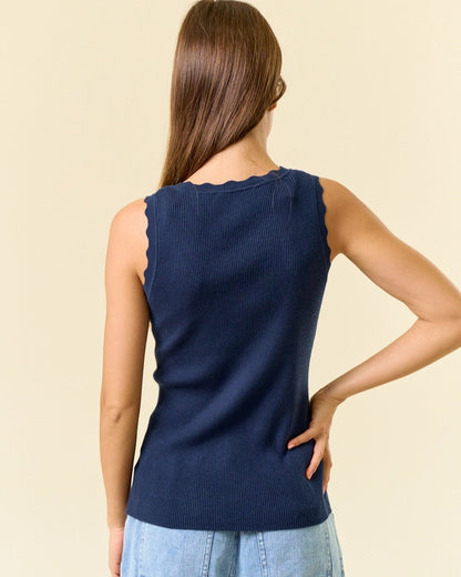 Woman wearing a navy sleeveless top and light blue jeans against a beige background.