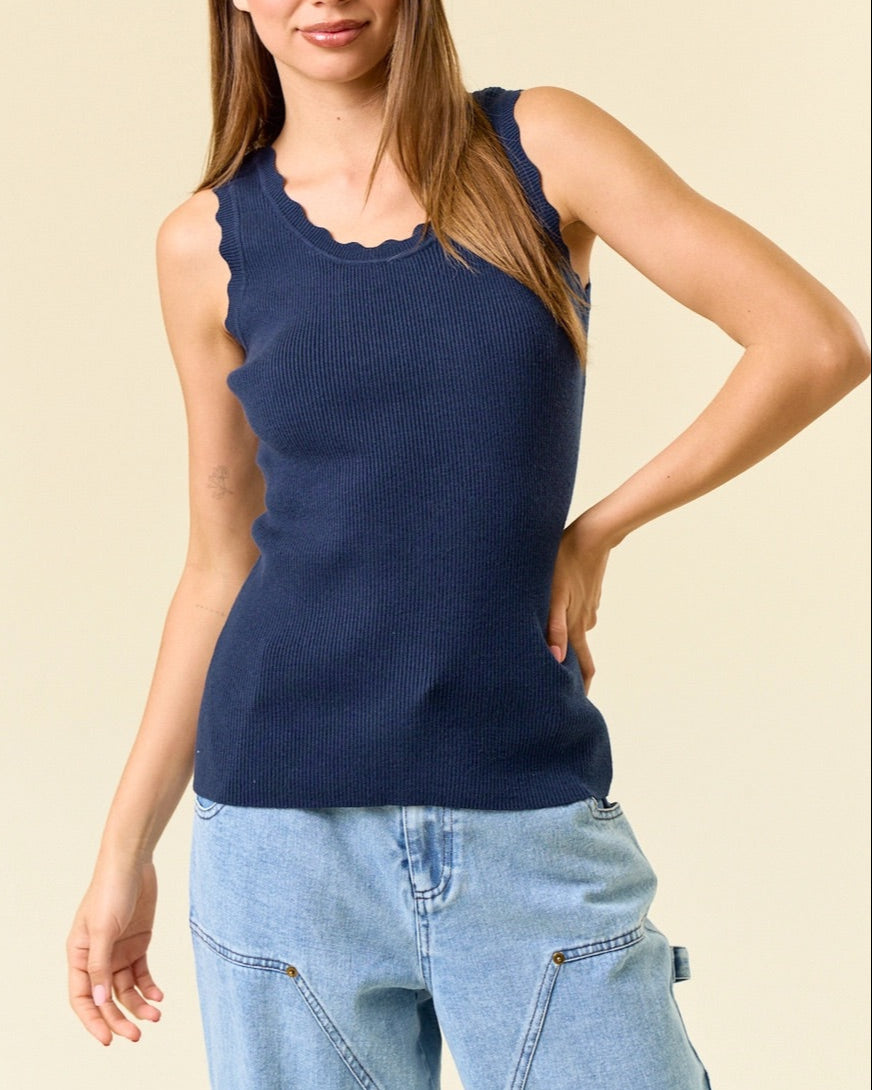 Woman wearing a navy blue sleeveless ribbed top and light blue jeans against a beige background.