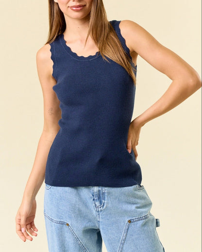 Woman wearing a navy blue sleeveless ribbed top and light blue jeans against a beige background.