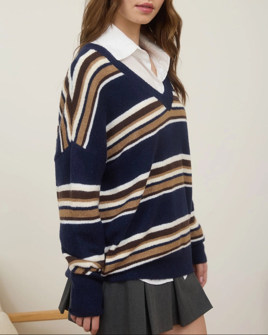 Woman wearing a navy, tan and white striped sweater with a white collared shirt against a plain background.