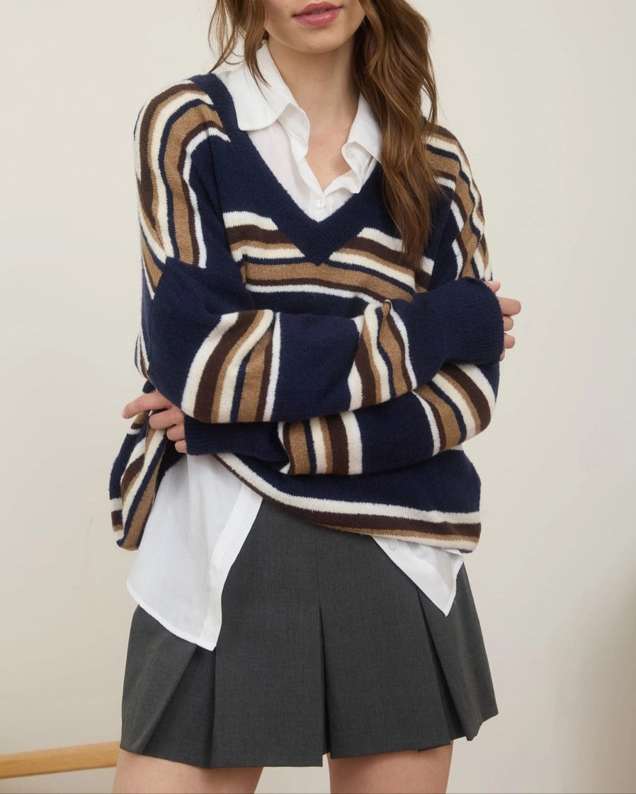 Woman wearing a striped sweater over a white shirt and gray skirt against a plain background. 