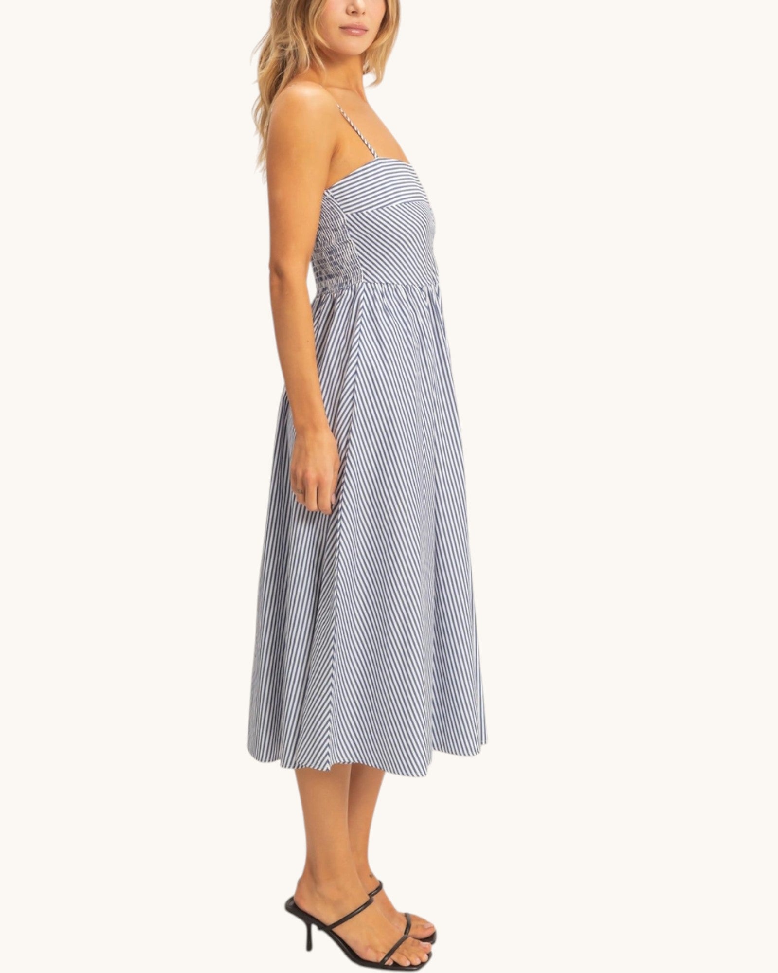 Side view of a woman wearing a blue and white striped dress and black strappy heels on a white background.