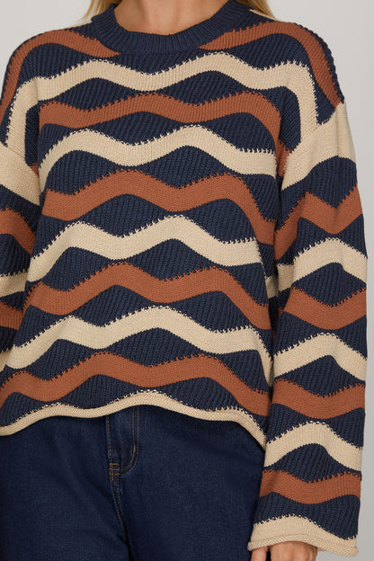 Close-up of ivory, navy, and cinnamon wave stripe knit sweater showing textured stitching, ribbed crew neckline, and rolled hem.