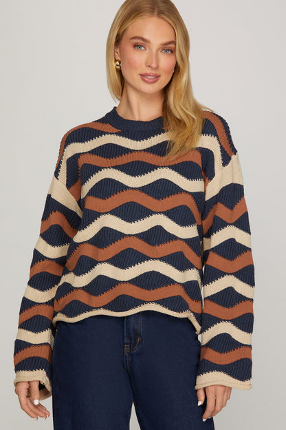Model wearing ivory, navy, and cinnamon wave stripe knit sweater with a relaxed fit, long sleeves, and rolled cuffs, front view.