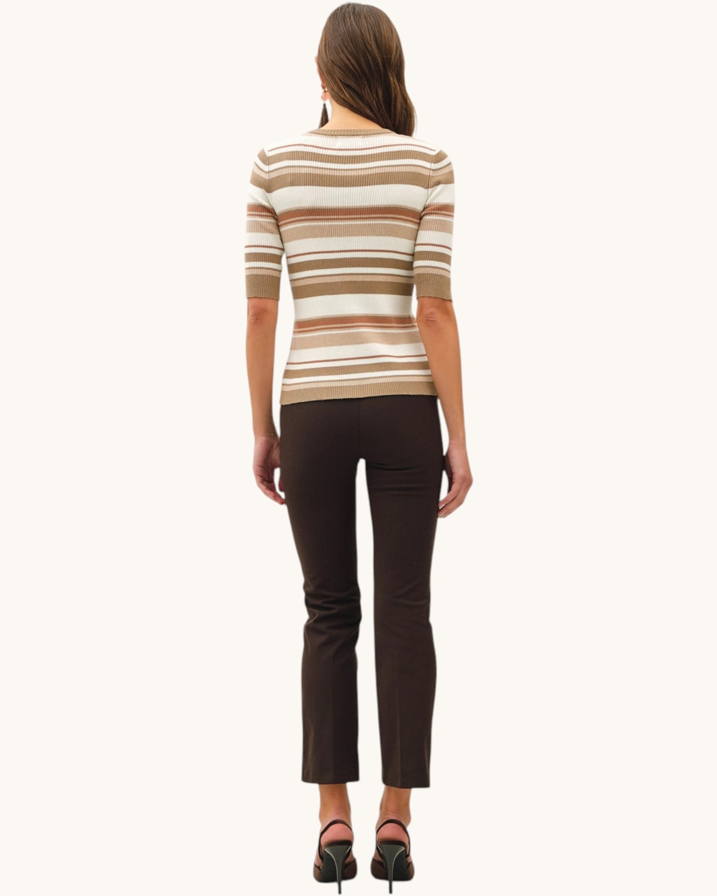 Woman wearing a striped sweater in warm earth tones and dark pants on a white background.