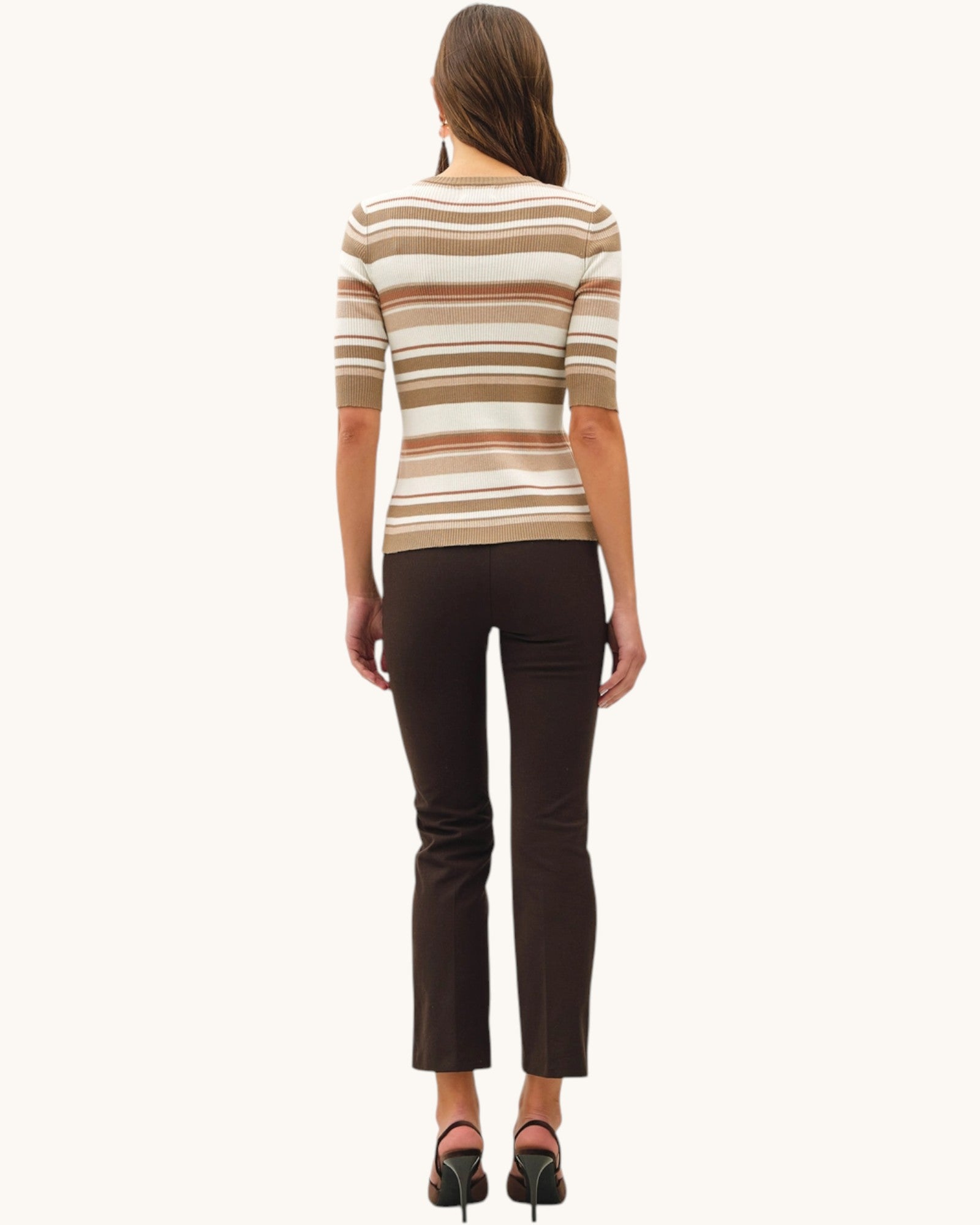 Woman wearing a striped sweater in warm earth tones and dark pants on a white background.
