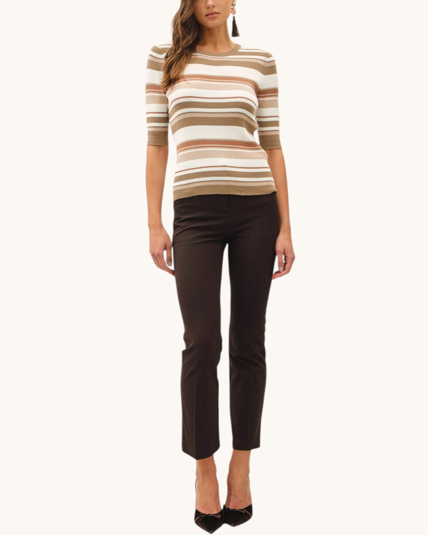 Woman wearing a earth toned striped sweater and black pants on a white background.